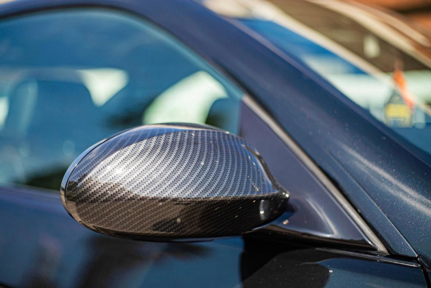 Close-up of a carbon fibre wing mirror on a blue car under harsh sunlight