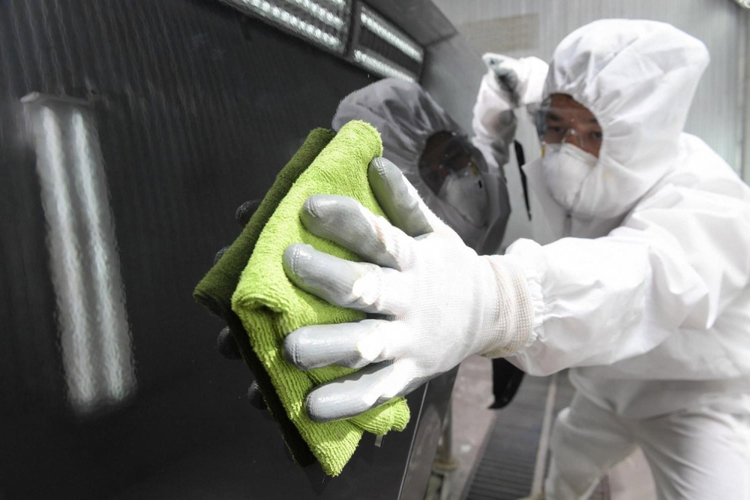 Technician in protective suit polishing a dark vehicle after paint correction